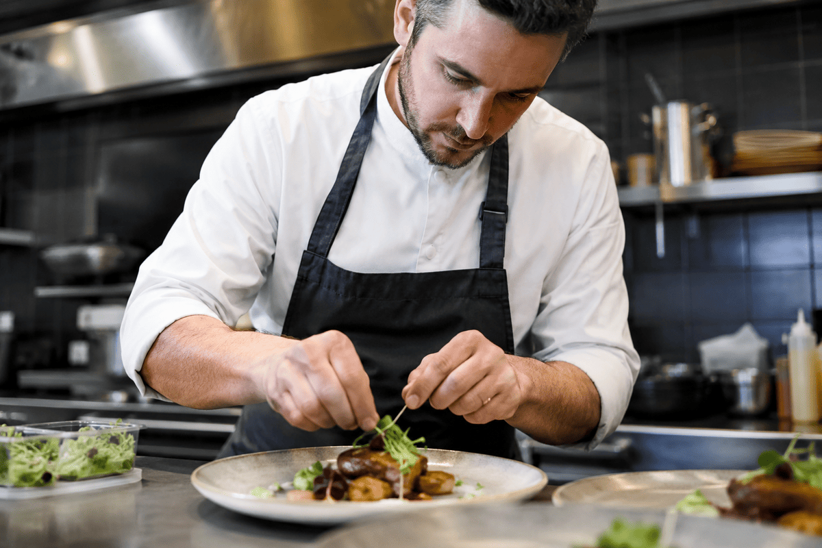 recruter un cuisinier : un cuisinier monte une assiette dans la cuisine du restaurant